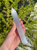 Selenit Massage Griffel mit Spitze- Akupunktur-Massagestab - 15cm in der Hand mit grünen Pflanzen im Hintergrund.