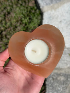 Orange heart-shaped selenite tealight holder, 9cm, known as a light bringer and protective stone, held in hand outdoors.